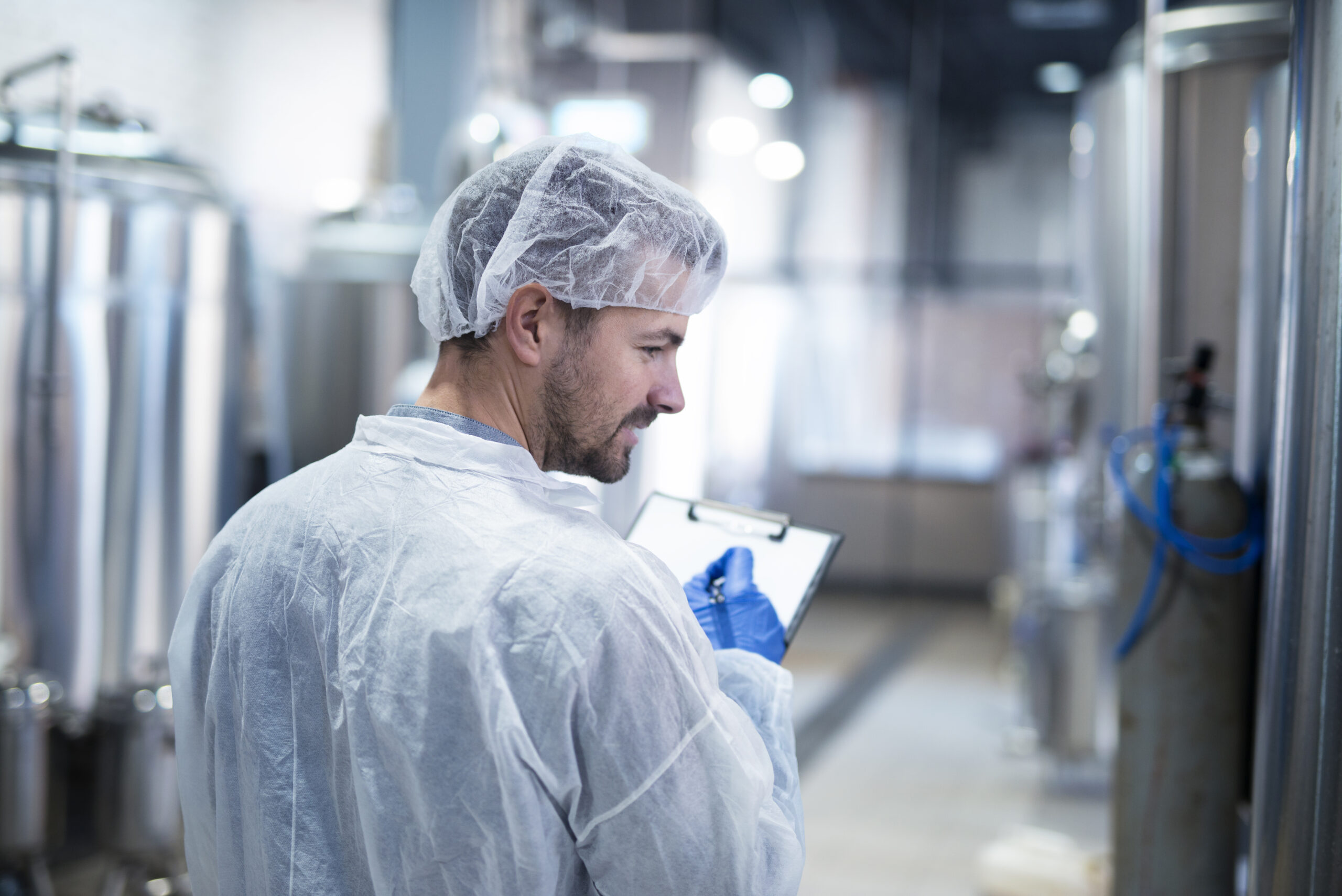 A technologist wearing a cleanroom suit monitoring and controlling pharmaceutical production inside a factory, ensuring compliance with industry standards.